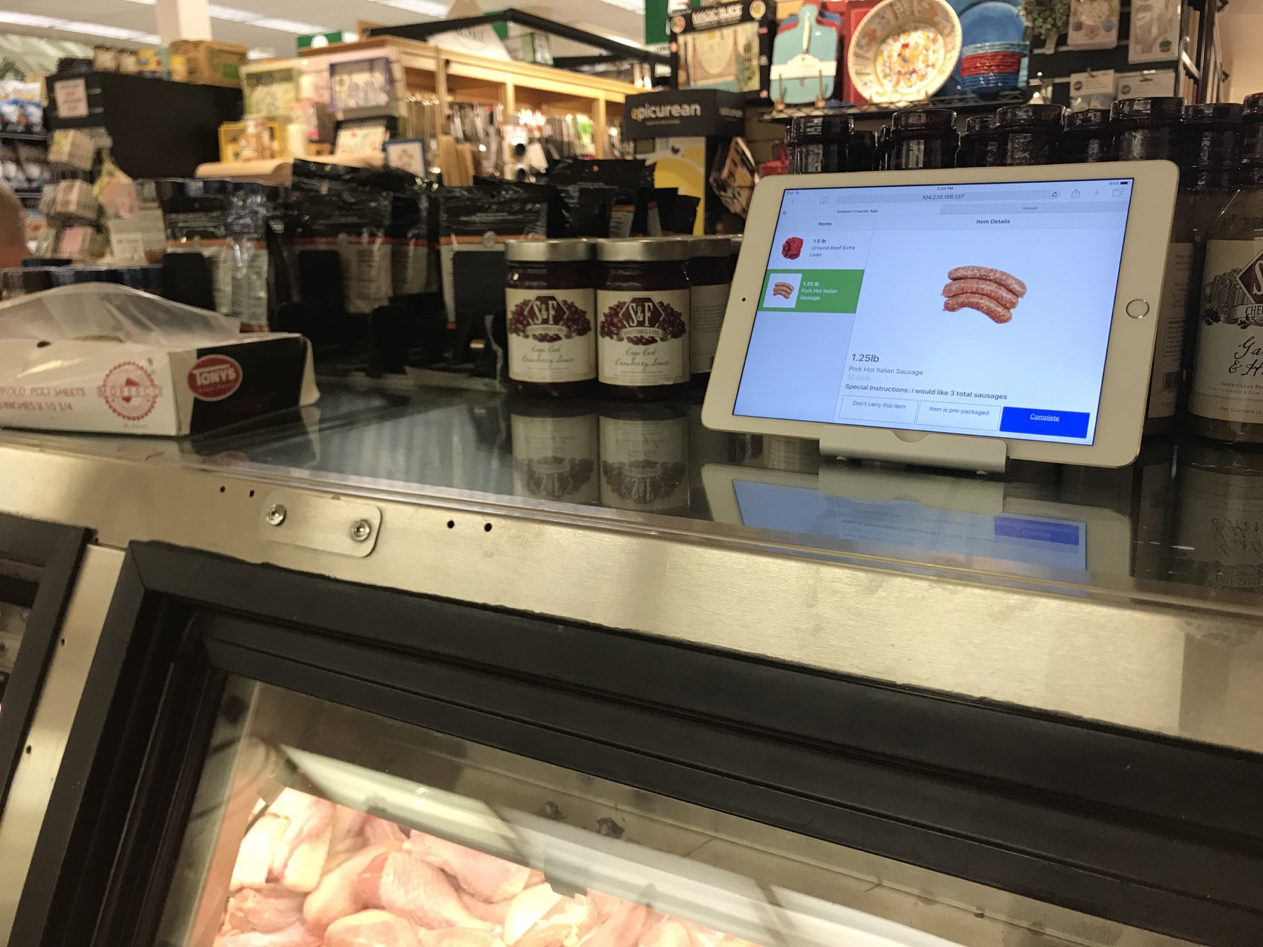 An iPad propped on a butcher counter running an early Instacart counter app, with a meat case below